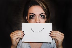 Person holding a smile drawn on paper while crying to symbolize coping with seasonal depression