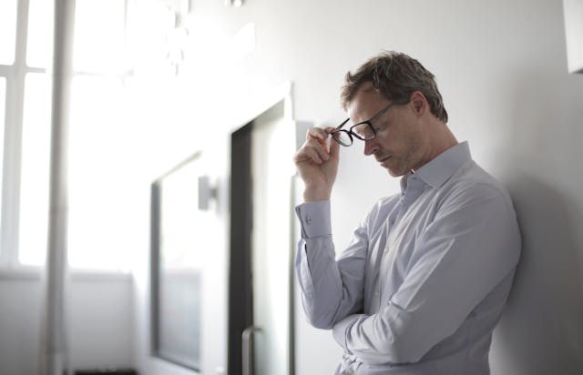 A stressed man taking off his glasses