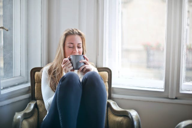 A woman in a white sweater drinking a cup of coffee.