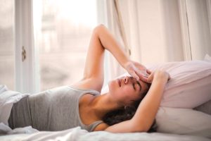 A woman lying in bed with her hands touching her forehead